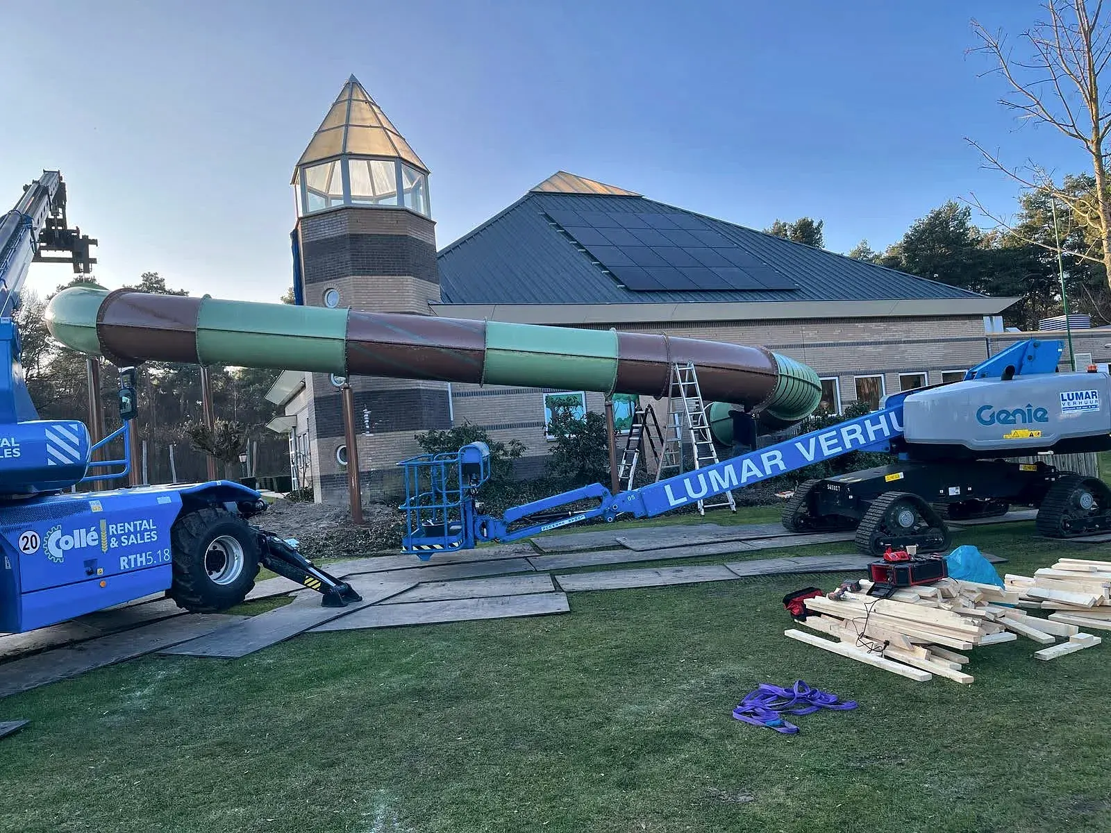 Montage van een glijbaan met hoogwerkers langs een zwembad