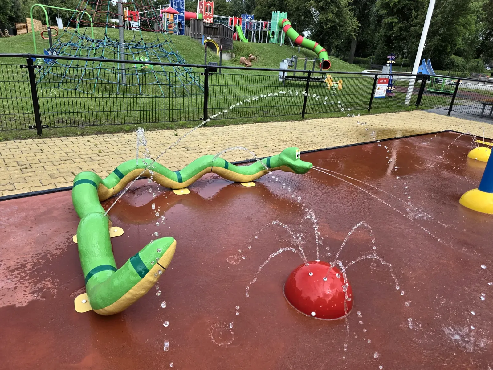 Slang-sproeier en rode koepelsproeier in werking op een spraypark